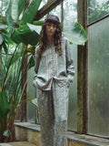 Person standing in a greenhouse with large plants and glass walls.