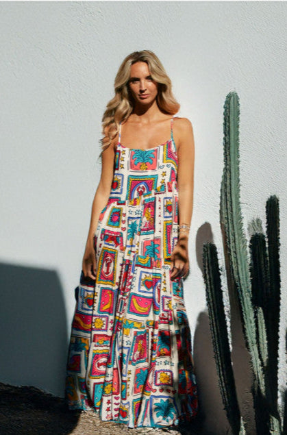 Woman wearing a colorful dress standing next to a cactus against a white wall